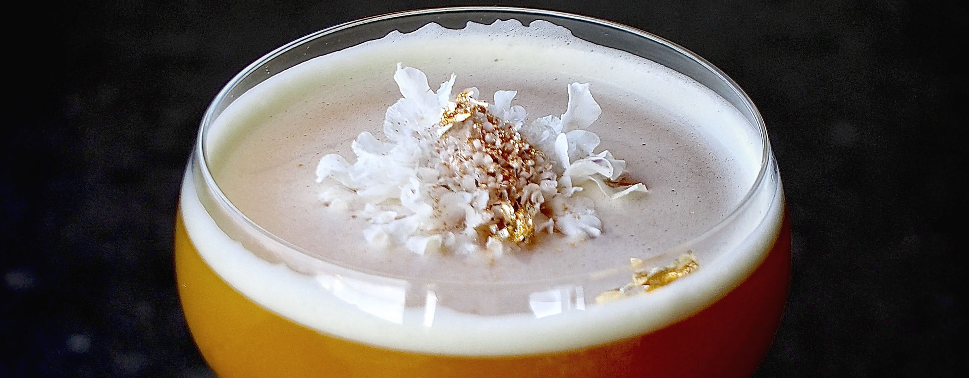Image of a cocktail with white foam and white and gold flower garnishes.