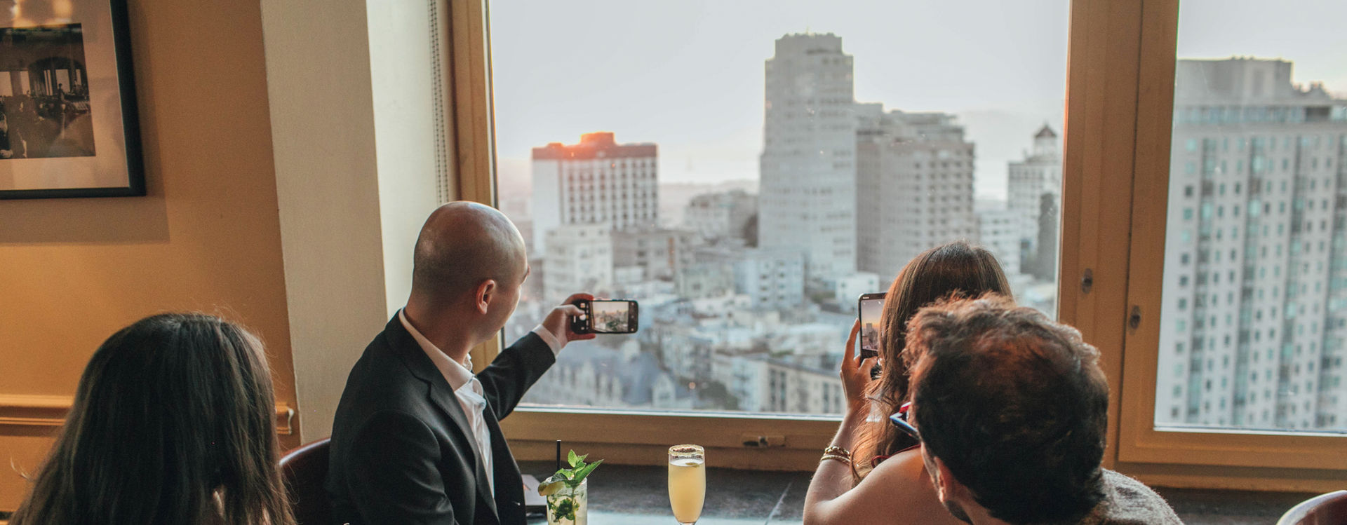 Guest at the Top of the Mark taking snapshots of the sun setting behind the Golden Gate Bridge.