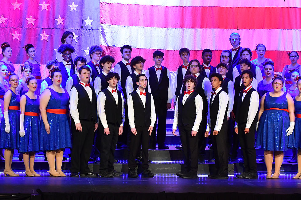 A photo of a group of students on stage singing "America The Beautiful" at the 2024 Rhapsodies Show Choir