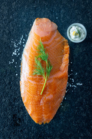 Geräuchertes Lachsfilet auf dunklem Untergrund mit Dillzweig und Creme mit Zitrone.