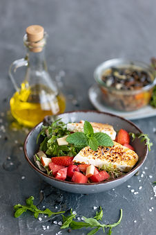 Food Photography des Restaurants Hora. Auf dem Bild ist ein Schüssel mit Käse, Salat und Wassermelonen zu sehen. im Hintergrund steht einen Olivenflasche.