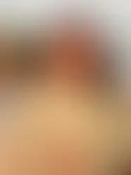 Portrait of a woman smiling outdoors on the deck of a boat by the river. She has long dark hair, is wearing a light green button-up shirt with a name tag that reads ‘Gaby,’ and stands with her arms resting on the railing. The river and a green forested shoreline are visible in the background under a partly cloudy sky.