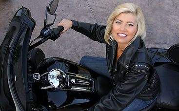 Environmental portrait of Brenda in motorcycle leathers beside her motorcycle on her patio.