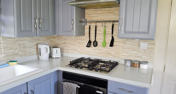 Clean compact kitchen with gas hob, oven, kettle and hanging utensils.