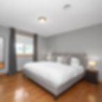 Spacious primary bedroom featuring cool gray walls, warm hardwood floors, an upholstered gray platform bed dressed in crisp white linens, matching bedside nightstands with warm lighting, and a long dresser.