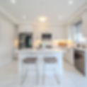 Bright, modern open-concept kitchen featuring light wood cabinetry, white marble-look tile floors, a center island with two bar stools, and stainless steel appliances.