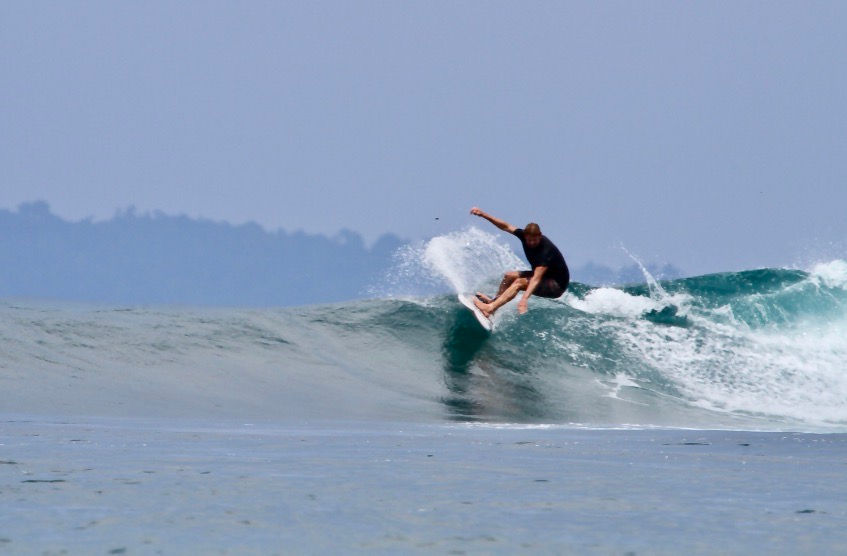 Surfer riding a small wave at Gunturs during the low season in the Bay of Plenty, Banyak Islands, Indonesia.