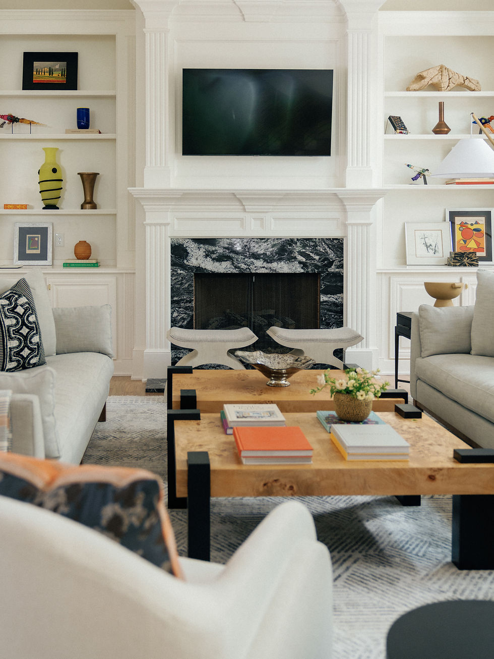 Atlanta living room design featuring a dramatic black marble fireplace, symmetrical white built-ins with curated art, burl coffee table, and neutral upholstered seating by Sarah Bowman Spaces