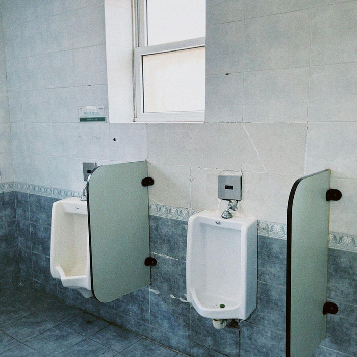 Tiled public restroom with two urinals and a window