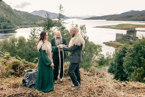 The officiant begins the handfasting ceremony during bride and groom's wedding ceremony with Eilean Donan Castle in the background