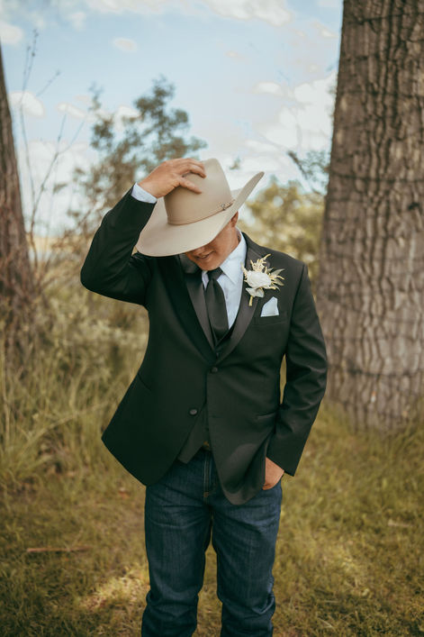 Groom tips his cowboy hat in this portrait on his wedding day