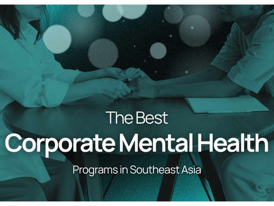 Two people hold hands across a table under teal lighting, with text: The Best Corporate Mental Health Programs in Southeast Asia.