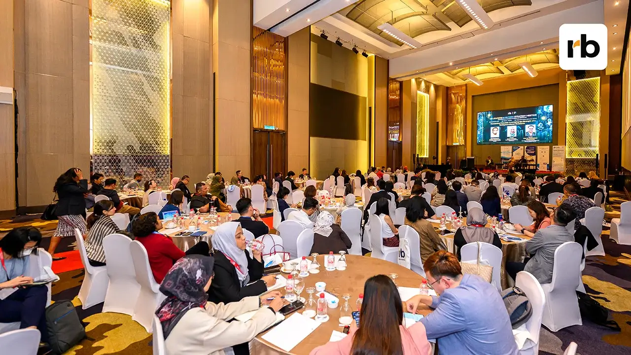 A diverse crowd of people sitting at tables in a big room, interacting and enjoying their time together.