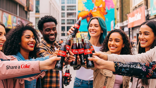 A group of friends smiles as they toast with Coke bottles in a vibrant urban setting. Bright mural background, text: "Share a Coke."