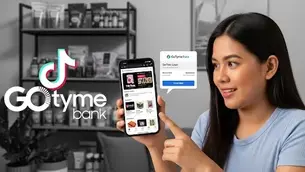 Woman smiling, pointing at smartphone displaying app in a room with shelves. GoTyme Bank and TikTok logos are visible.