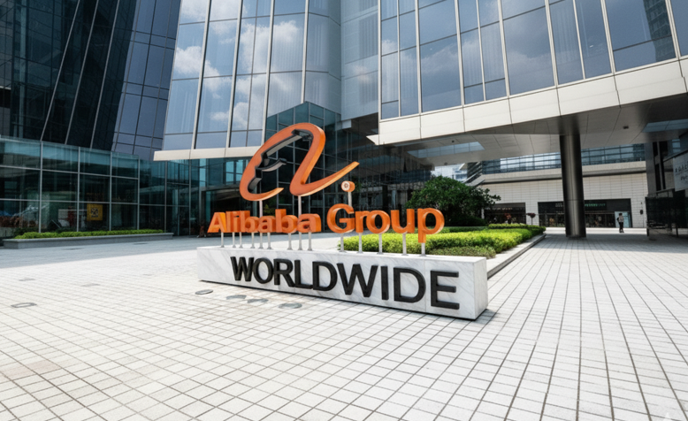 Alibaba Group sign with orange logo on a marble base reading "WORLDWIDE," set in a modern office building exterior with glass facades.