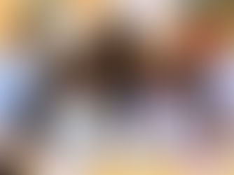 Five people smiling, gathered around a laptop in a brightly lit office with colorful charts on the wall. Mood is collaborative and cheerful.