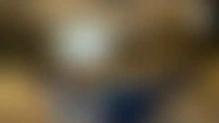 Audience in a conference room listening to a presenter in pink under chandeliers. Presentation slide with text, round tables, neutral tones.