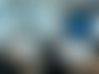 Office scene with people at desks working on computers. Multiple screens display charts and graphs. Bright, modern workspace.