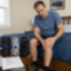 Person sitting on the edge of a bed holding their knee in pain, considering different knee brace options