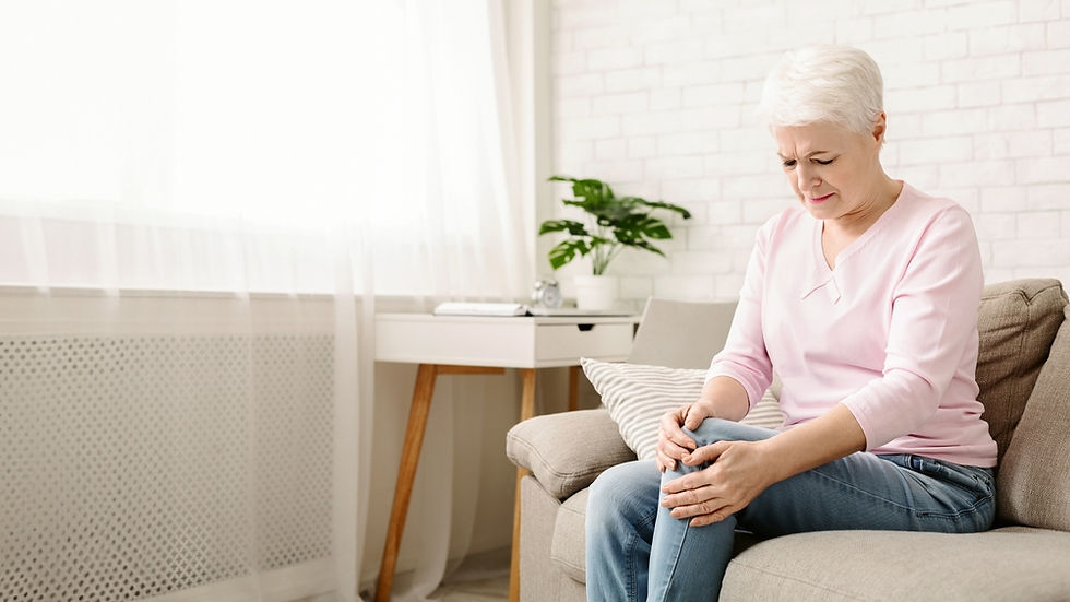 Elderly woman clutching knee osteoarthritis pain on couch. 