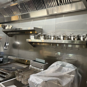 Stainless steel commercial kitchen with grill and shelves.