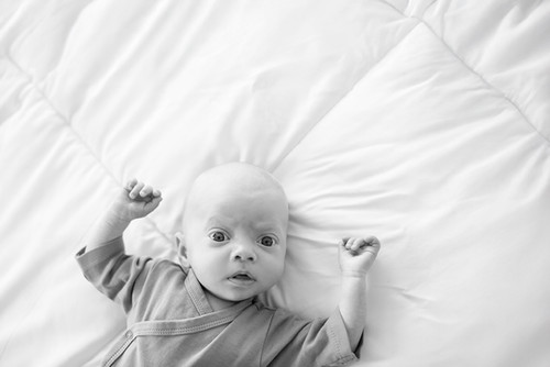 A young baby lying on a bed looking up at the camera in a lifestyle sesion