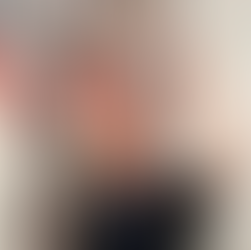 A man in glasses raises his hand in front of an abstract painting with red, black, and gray tones.