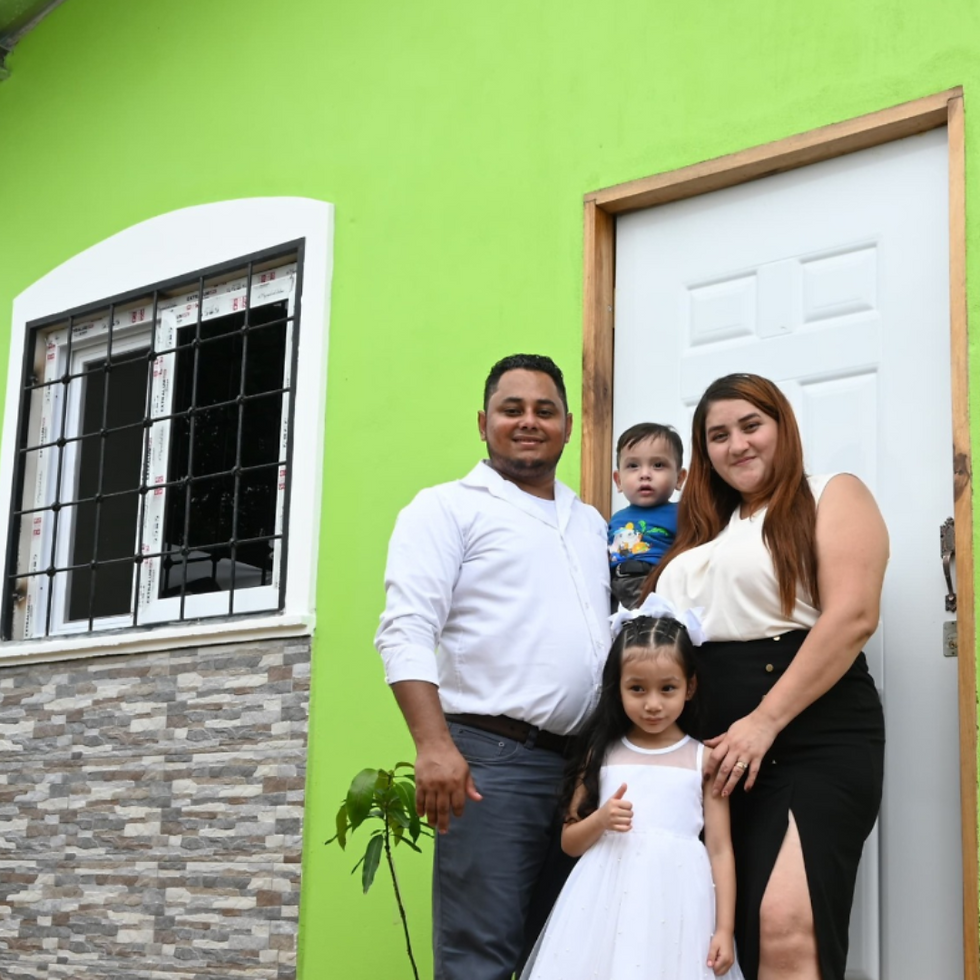 A family stand in front of a green house.