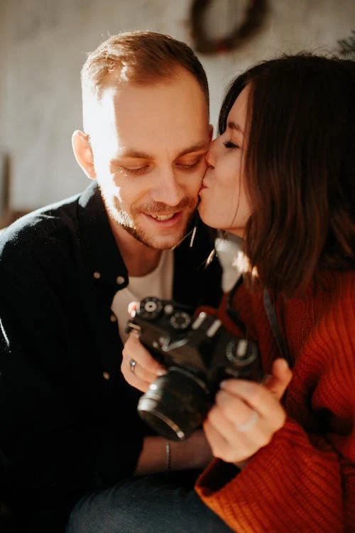 image of wife kissing husband on the cheek as they look at the image he took of her