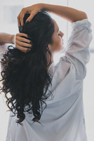 A Latina woman with black hair in a white collared shirt posing in front of a window during her therapeutic photo session in Irvine boudoir studio