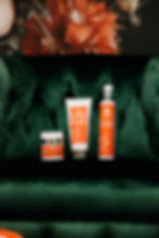 Three medical grade skincare bottles with orange labels on a dark green velvet couch, set against a floral background. Text includes "Hydration Haven". Items include a moisturizer, a 10% BPO acne cleanser, and an antioxidant green tea gentle cleanser ideal for dry, sensitive or mature skin.