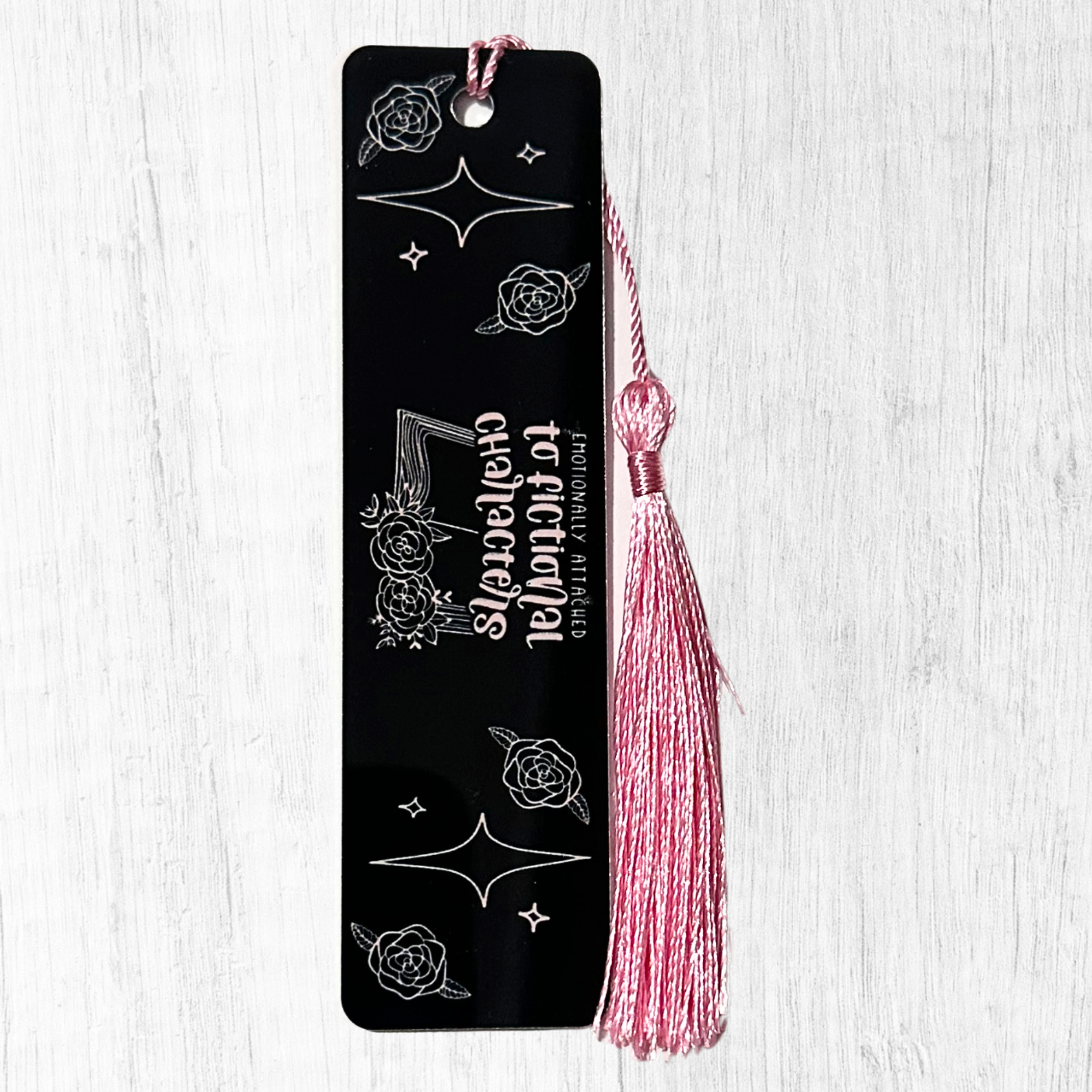 Black bookmark with white text about being emotionally attached to fictional characters and pink tassel
