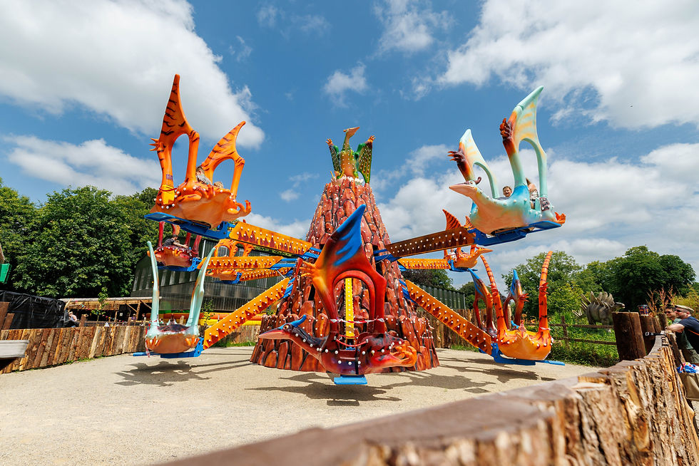 Jurassic Newpark Colorful dinosaur-themed amusement ride spins under a blue sky, with riders smiling in orange and teal seats.