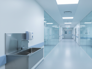 Corredor hospitalar moderno com foco em uma pia de higienização de aço inoxidável brilhante.