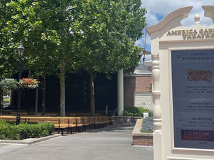 Open air amphitheater with trees intermingles with bench seating. American Garden theater sign is in the forefront.