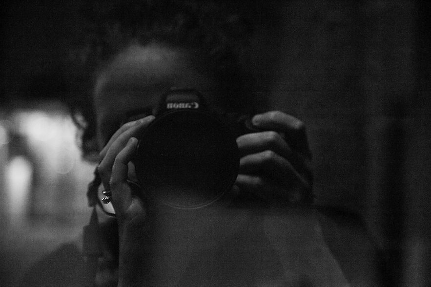 Reflected black and white photograph of Katie Adkins holding a Canon camera lens