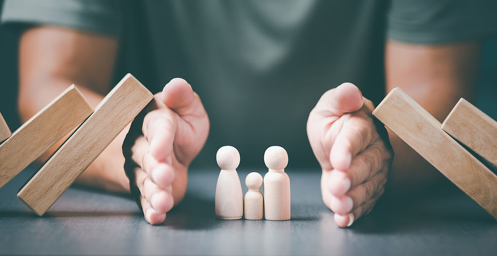 Hands protect wooden figures of a family from falling blocks, symbolizing protection and care. Neutral colors create a calm mood.