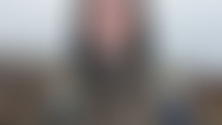 A young man in a waterproof coat and backpack smiles at the camera