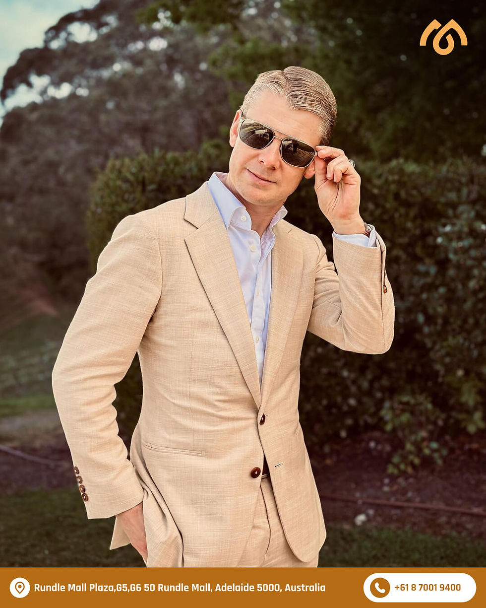 Man wearing a beige tailored suit and sunglasses from a formal wear shop in Adelaide, showcasing modern bespoke menswear style.