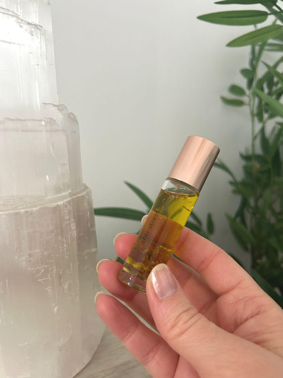 Main tenant un roll-on aux huiles essentielles d’agrumes devant une lampe de sélénite et une plante de bambou, pour soutenir l’énergie émotionnelle en hiver