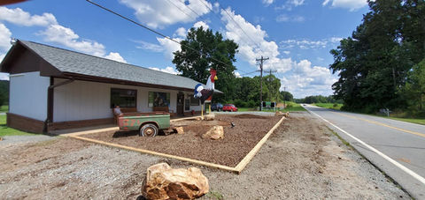 Landscaping workers spreading mulch around a large chicken sculpture near a commercial building