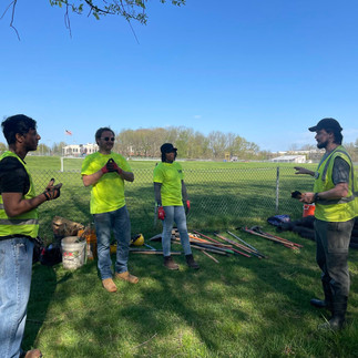 Uplift Crew w/ field tech. Team wearing high visable clothing gathered in a field, while field tech gives directions