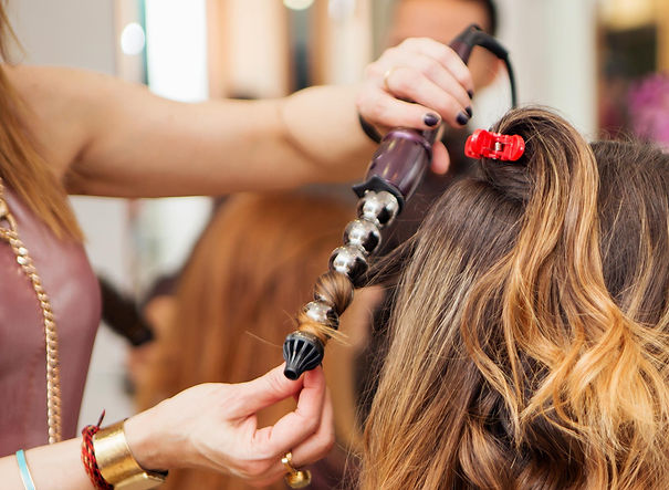 Hairdresser using curling tongs on customers long brown hair in salon