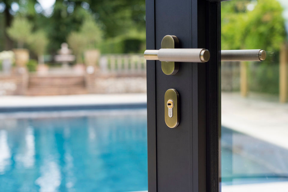 Close up of Origin bi-fold door hardware and swimming pool in the background