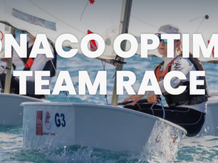 Tre bambini su una barca Optimist con vela bianca durante una regata nella Baia di Monaco, gara sportiva giovanile.