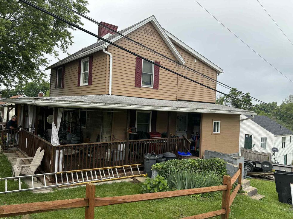 Two-story beige house with porch, fence, and green grass on a cloudy day.