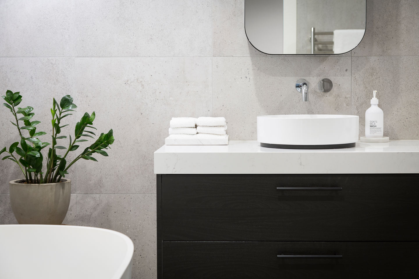 Modern bathroom sink with towels and plant on a white countertop setting.