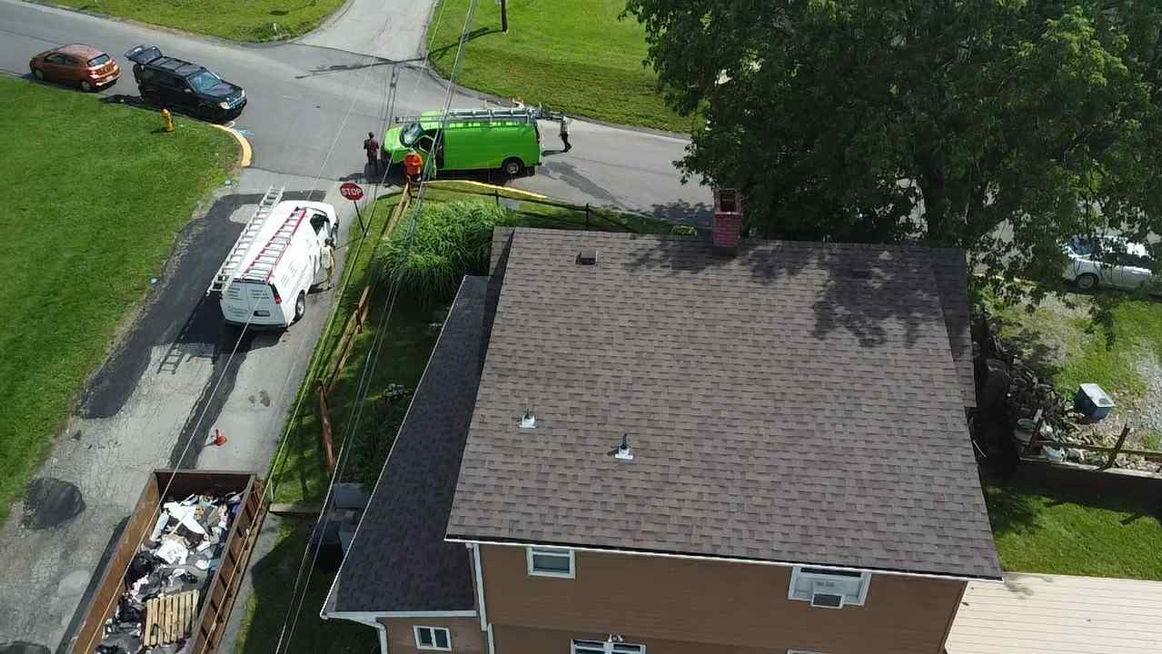 Roofers working on a home with vans and debris nearby, aerial view