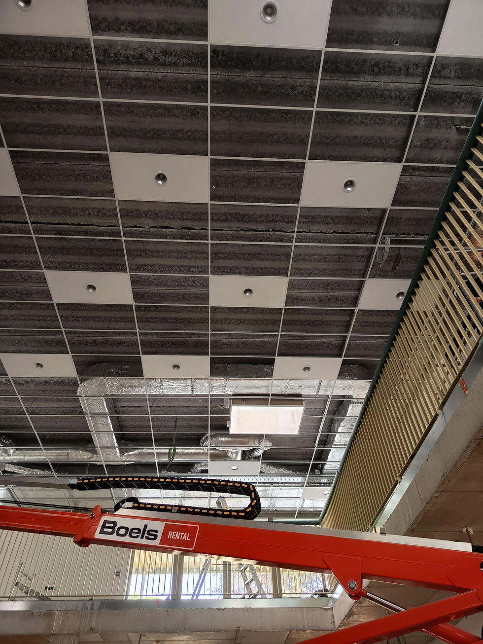 In de centrale dubbelhoge projectruimte wordt de structuur van het plafond opgehangen met bevestiging van de akoestische inlegtegels en de verlichtingsarmaturen.